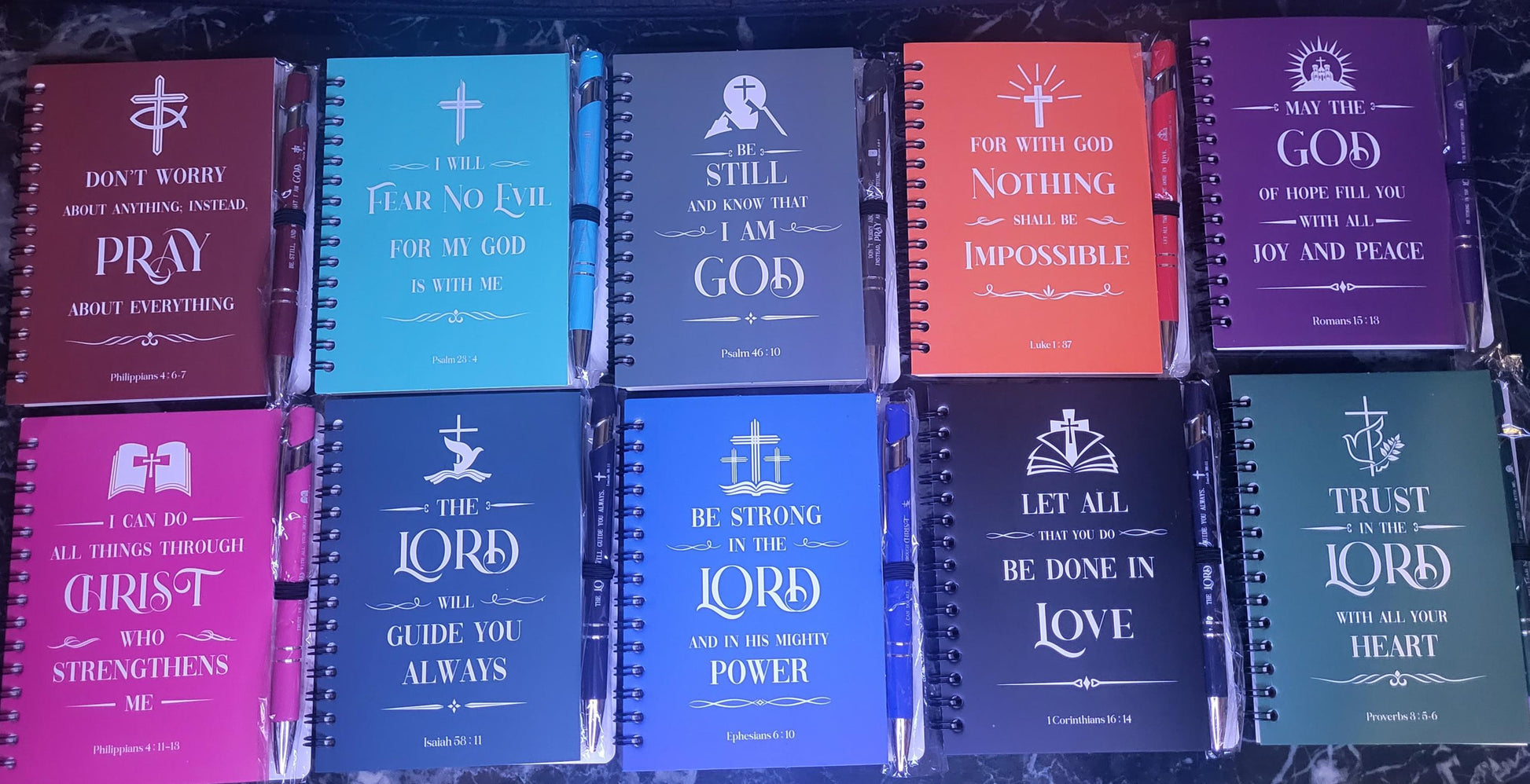 Colorful spiral notebooks with matching sturdy pens displaying Christian bible verses